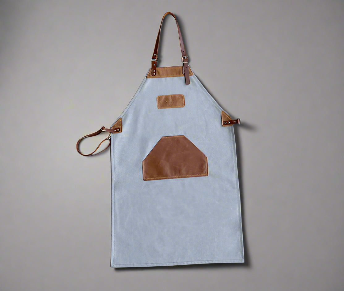 Grey and tan canvas and leather apron with adjustable cross-back straps and utility pockets, handmade in Cape Town. Available for custom branding.