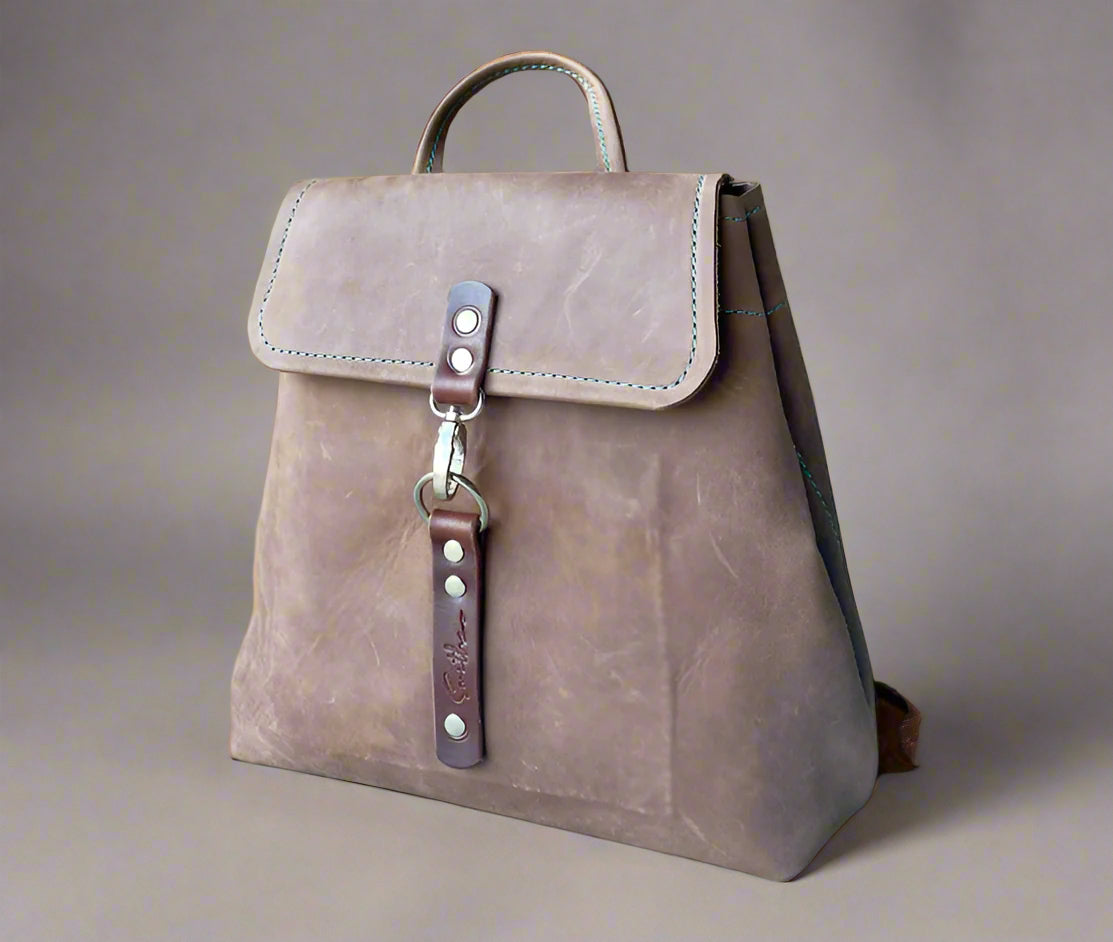 Compact full grain leather backpack in brown with sturdy veg tan shoulder straps and a secure outer easy access pocket. Handmade by women in Cape Town.