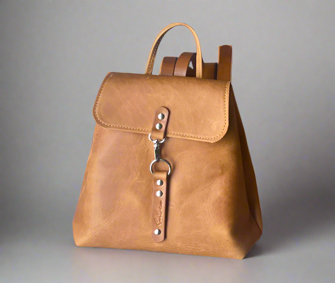 Compact full grain toffee coloured leather backpack with sturdy veg tan shoulder straps and a secure outer easy access pocket. Handmade by women in Cape Town.