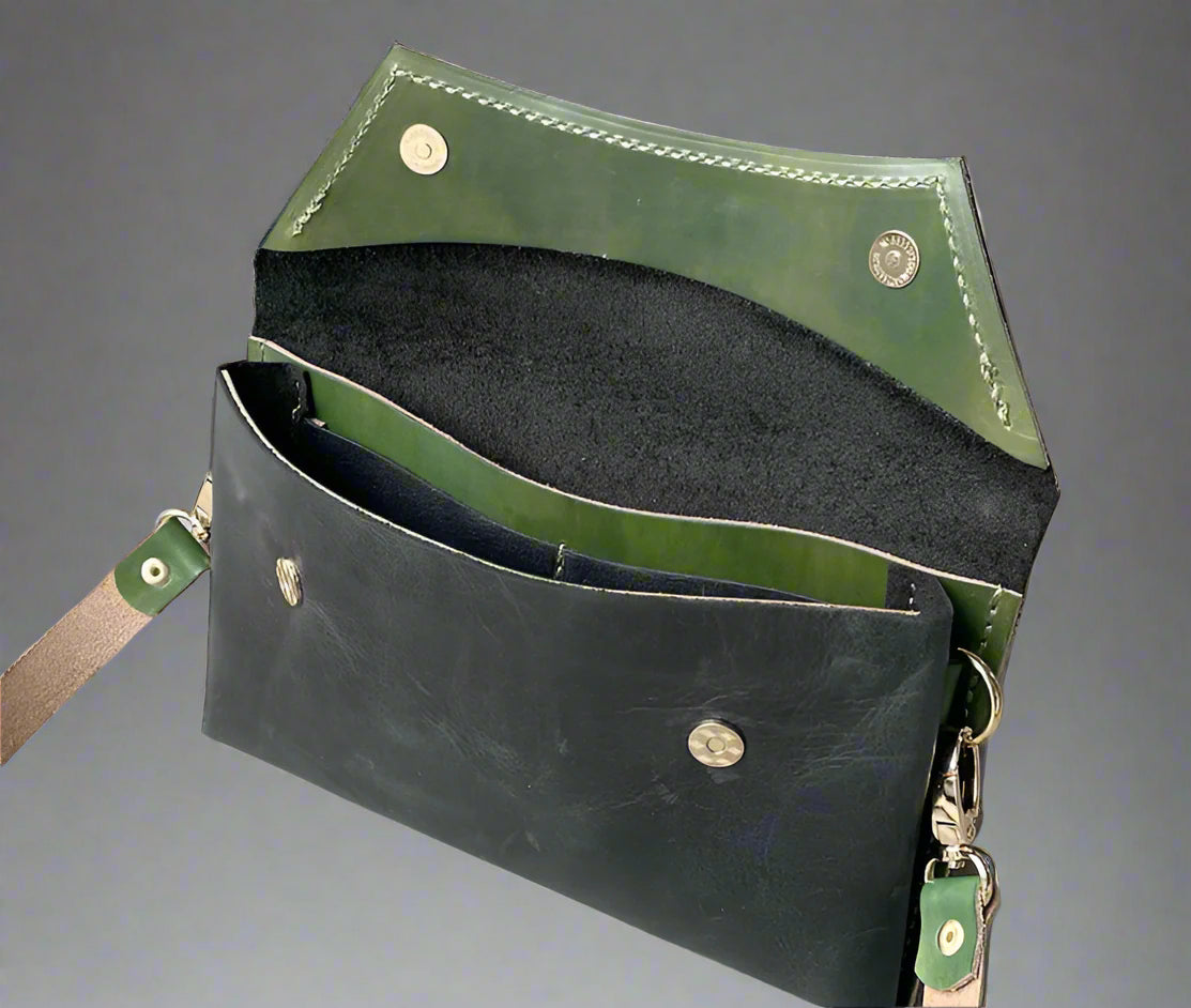 A black full grain leather clutch sized bag with green coloured detail, stunning curved lines, and studs along the base.