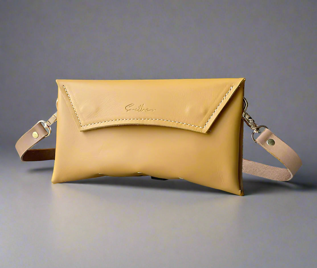 An ochre yellow  full grain leather clutch sized bag with natural coloured detail, stunning curved lines, and studs along the base.