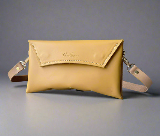An ochre yellow  full grain leather clutch sized bag with natural coloured detail, stunning curved lines, and studs along the base.