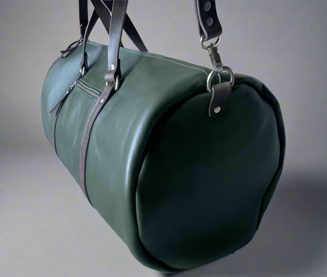Green leather duffel bag with brown straps on a stone surface.