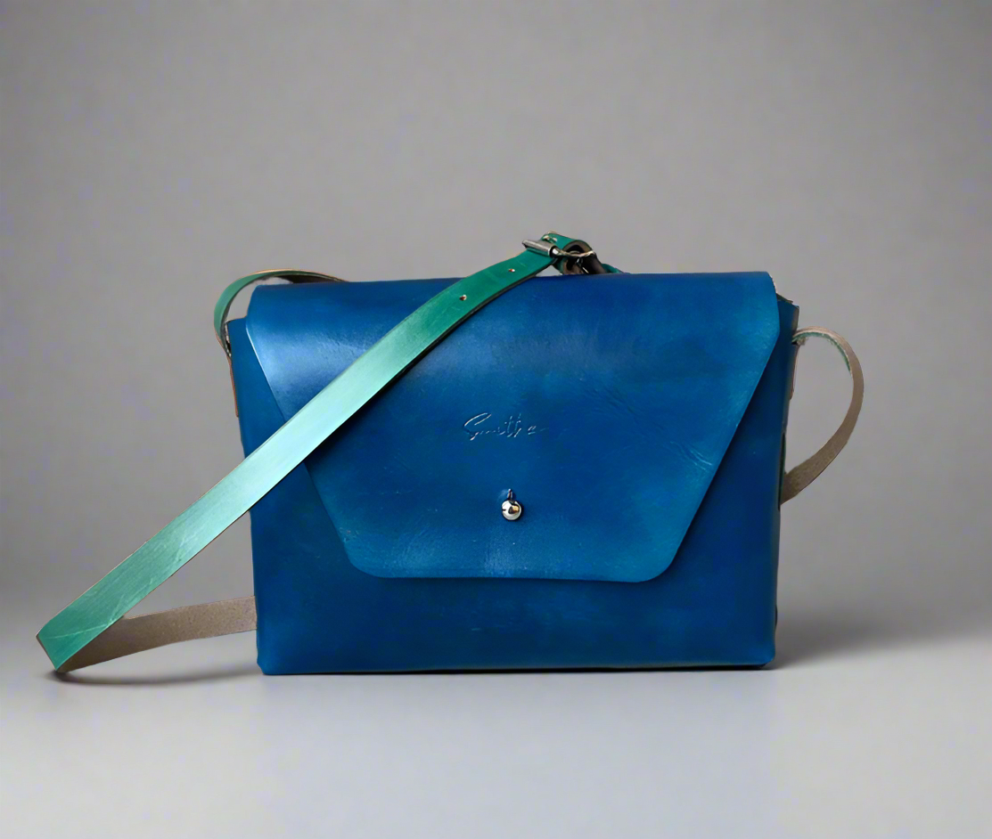 Smooth full grain hand-dyed leather crossbody bag with raw edges and no stitching, handmade in Cape Town. Available in blue with turquoise detail.
