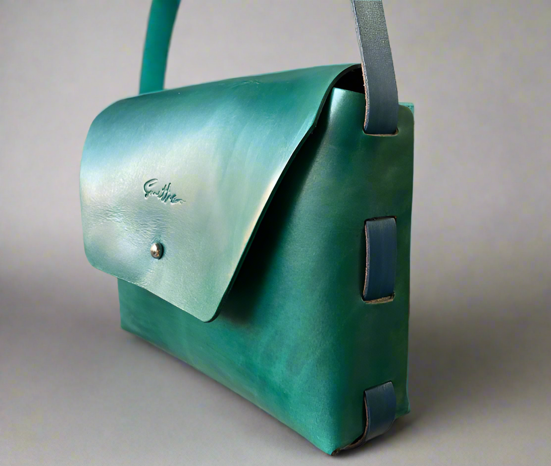 Smooth full grain hand-dyed leather crossbody bag with raw edges and no stitching, handmade in Cape Town. Available in turquoise with blue detail.