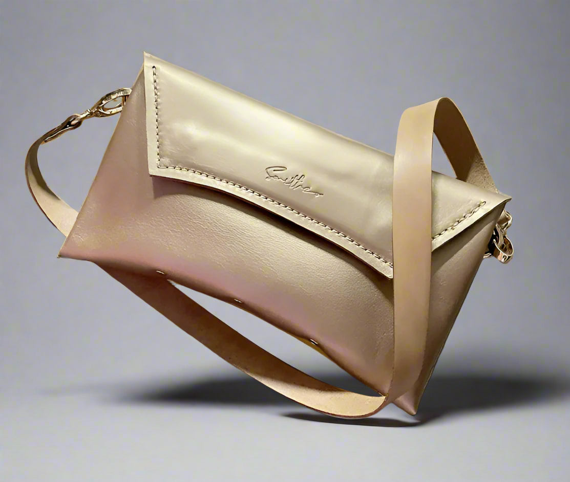 A gold full grain leather clutch sized bag with natural coloured detail, stunning curved lines, and studs along the base.
