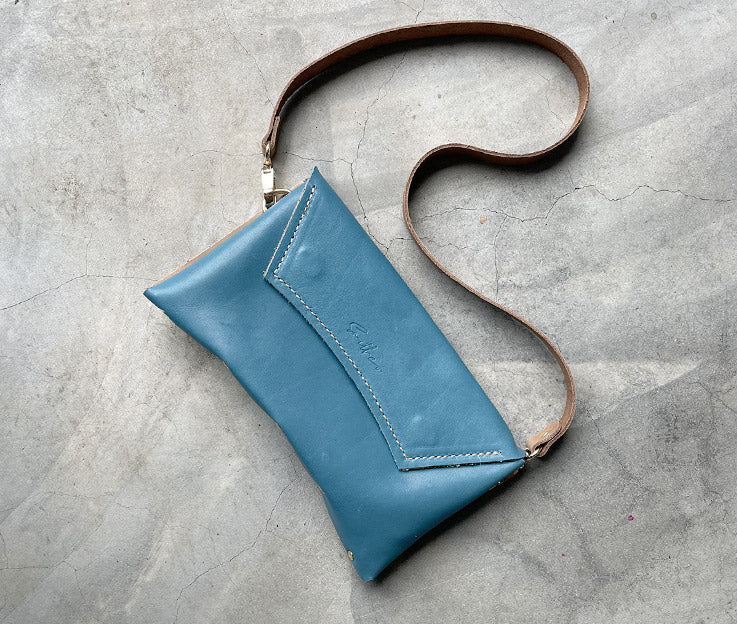 Handmade full-grain dusty blue leather Crescent Clutch Bag with muted two-toned design – versatile clutch or crossbody with adjustable strap. Perfect for stylish women, features compartments for phone and cards.