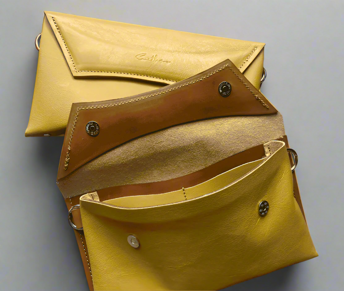 Two ochre yellow full grain leather clutch sized bag with tan coloured detail, stunning curved lines, and studs along the base.
