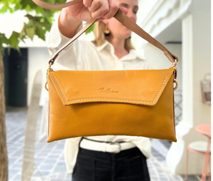 A person holding a yellow crescent clutch bag with a shoulder strap and a zipper closure.