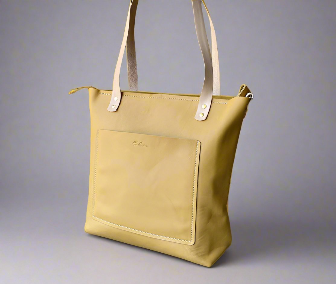 Handmade ochre yellow leather shopper bag crafted from full-grain leather. Features a front stitched pocket with embossed branding, a secure zip closure, and natural-tone double handles for easy carrying. A stylish and durable leather tote bag perfect for daily use, shopping, or work essentials.