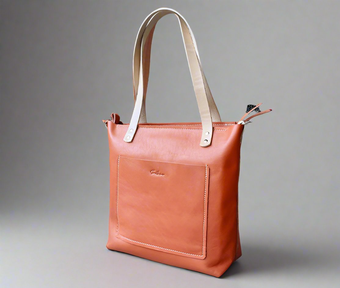 Handmade orange leather shopper bag crafted from full-grain leather. Features a front stitched pocket with embossed branding, a secure zip closure, and natural-tone double handles for easy carrying. A stylish and durable leather tote bag perfect for daily use, shopping, or work essentials.